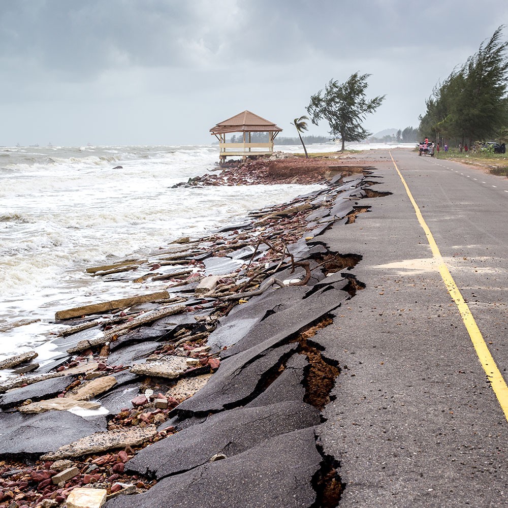 A road eroding along the coastline with a cloudy sky and life guard tower in the background