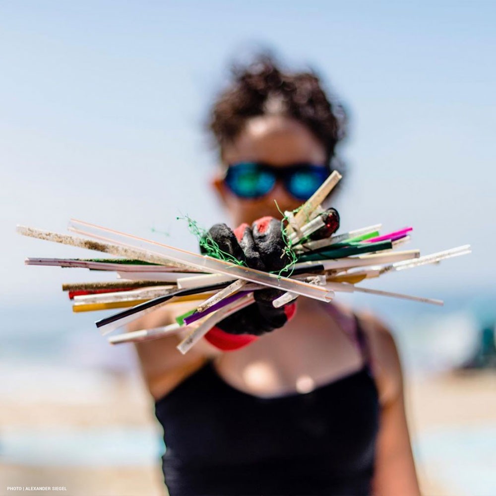 Volunteer on beach holds up a handful of plastic straws from a cleanup event