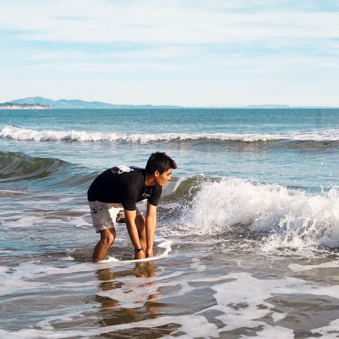 Man reaches hands down into the shallow ocean water.