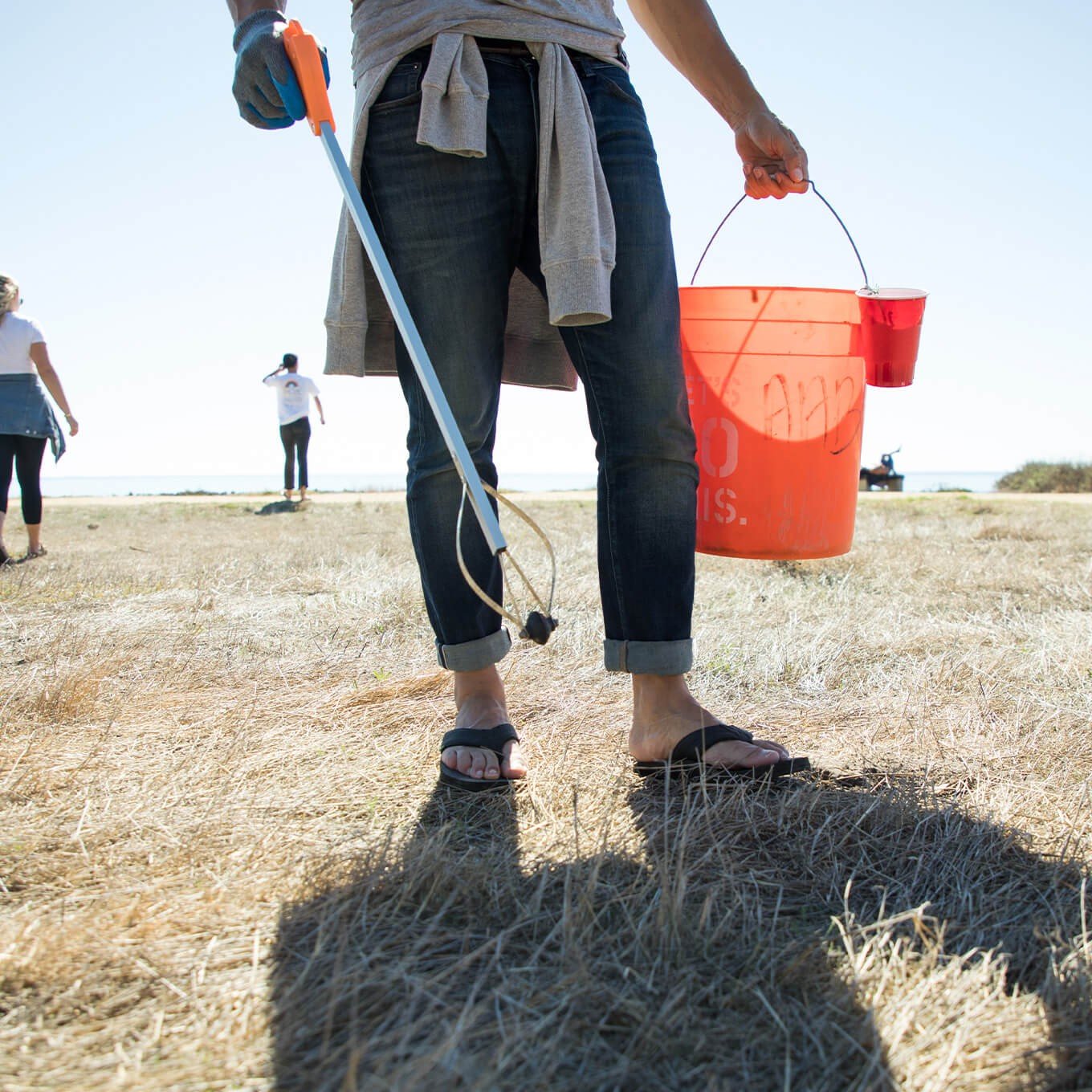 A volunteer uses a bucket and grabber to collect beachside litter.